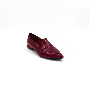 May include: A pair of burgundy leather loafers with a pointed toe and a buckle detail.