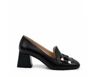 Könnte beinhalten: Ein schwarzer Loafer-Pumps aus Leder mit quadratischer Zehenpartie, einem klobigen Blockabsatz und einem dekorativen goldfarbenen Metallbeschlag über dem Vorderblatt. Der Schuh hat eine glatte Oberfläche und ein beiges Innenfutter.