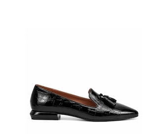 May include: A black patent leather loafer with a crocodile-embossed texture, featuring a pointed toe, a decorative tassel on the vamp, and a low, block-shaped heel. The interior lining of the shoe is a contrasting brown leather.