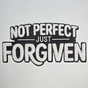 May include: A black and white patch with the words "NOT PERFECT" above "JUST" and "FORGIVEN" in a bold, textured font. The patch has a black border and is set against a white background.