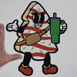 May include: A cartoon-style patch in the shape of a slice of pizza, with red and white stripes, holding a green drink. The patch has black eyes, a smiling mouth, and is wearing a brown bag. The patch has black legs and red shoes.