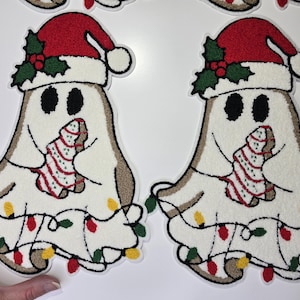 May include: Two Christmas-themed ghost-shaped decorations. Each ghost wears a red Santa hat with holly and holds a gingerbread tree. They are outlined in brown and decorated with colorful Christmas lights.