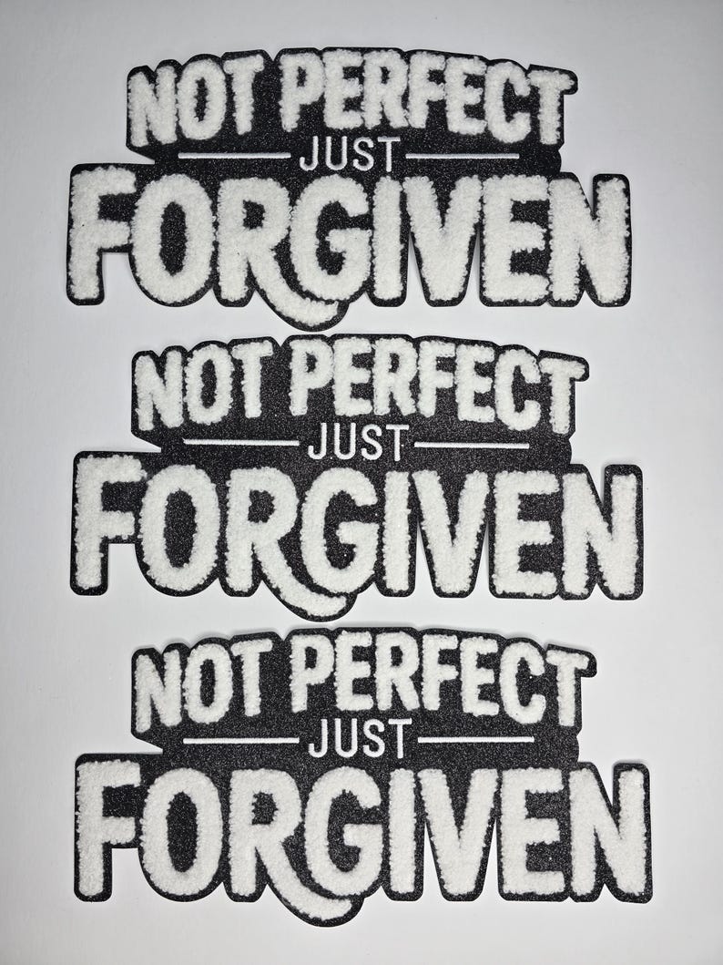 May include: Three black and white patches with the text "NOT PERFECT - JUST - FORGIVEN". The text is in a bold, stylized font with a fuzzy, white texture, set against a black background. The patches are arranged vertically.
