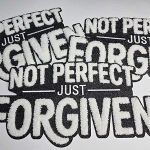 May include: Black and white patches with the text "NOT PERFECT JUST FORGIVEN". The text is in a bold, textured white font against a black background. The patches are cut in the shape of the text.