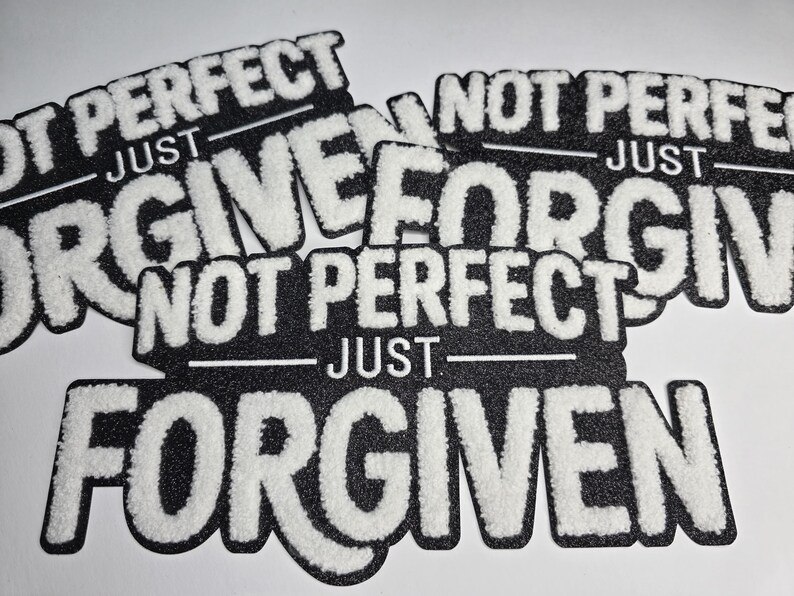 May include: Black and white patches with the text "NOT PERFECT JUST FORGIVEN". The text is in a bold, textured white font against a black background. The patches are cut in the shape of the text.