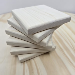 May include: A stack of six unfinished, square wooden coasters. The coasters are light-colored, with visible wood grain, and have slightly rounded edges. They are arranged in a spiral pattern on a light wood surface.