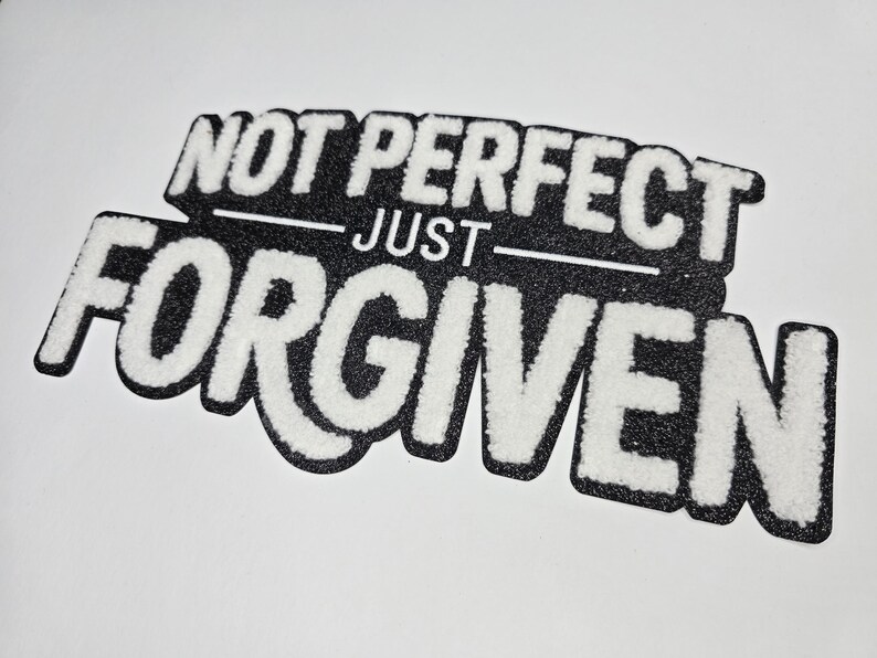 May include: A black and white patch with the words "NOT PERFECT JUST FORGIVEN". The text is in a bold, stylized font with a fuzzy, textured appearance. The patch is on a white background.