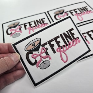 Peut inclure: Écusson brodé avec les mots "Caffeine Queen" en marron et rose, avec un motif de verre à martini. L'écusson a une bordure noire et est sur fond blanc. Plusieurs écussons sont visibles.