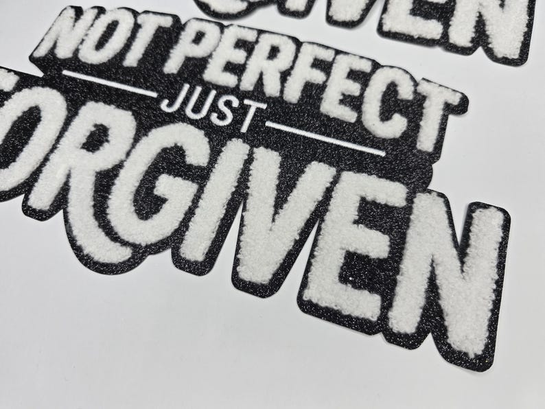 May include: Black and white embroidered patch with the words "NOT PERFECT JUST FORGIVEN". The text is in a bold, stylized font with a fuzzy, textured appearance. The patch has a black border.