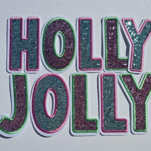 May include: Embroidered patches spelling "HOLLY JOLLY" in teal, burgundy, and green sequins. The letters have a white border and are set against a white background. Festive holiday decor.