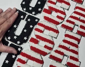 May include: Patches spelling "USA". The letter "U" is black with white stars, while the letters "S" and "A" have red and white stripes. The patches have a silver border.