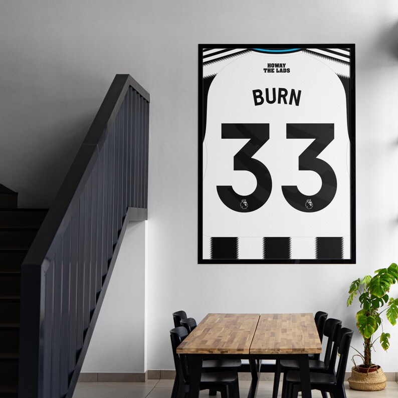 May include: Framed print of a white and black soccer jersey with the name "BURN" and the number "33" in black. The jersey has the text "HOWAY THE LADS" at the top. The print is displayed on a white wall.