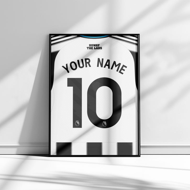 May include: Framed soccer jersey art print. The white jersey features a black number 10 and the text "YOUR NAME" above it. The words "HOWAY THE LADS" are at the top. The jersey is framed in a black frame.