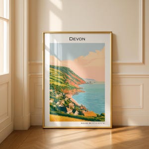 Könnte beinhalten: Ein vertikaler gerahmter Kunstdruck mit einer Küstenlandschaft von Devon, England. Die Illustration zeigt grüne Klippen, ein blaues Meer und kleine Häuser entlang der Küste unter einem sanften Himmel. Der Text DEVON steht oben, Koordinaten unten.