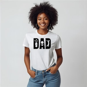 May include: White t-shirt with the word "DAD" in bold black letters. The letter "D" features a golf bag with clubs, the "A" has a golf ball, and the final "D" shows a golfer swinging.