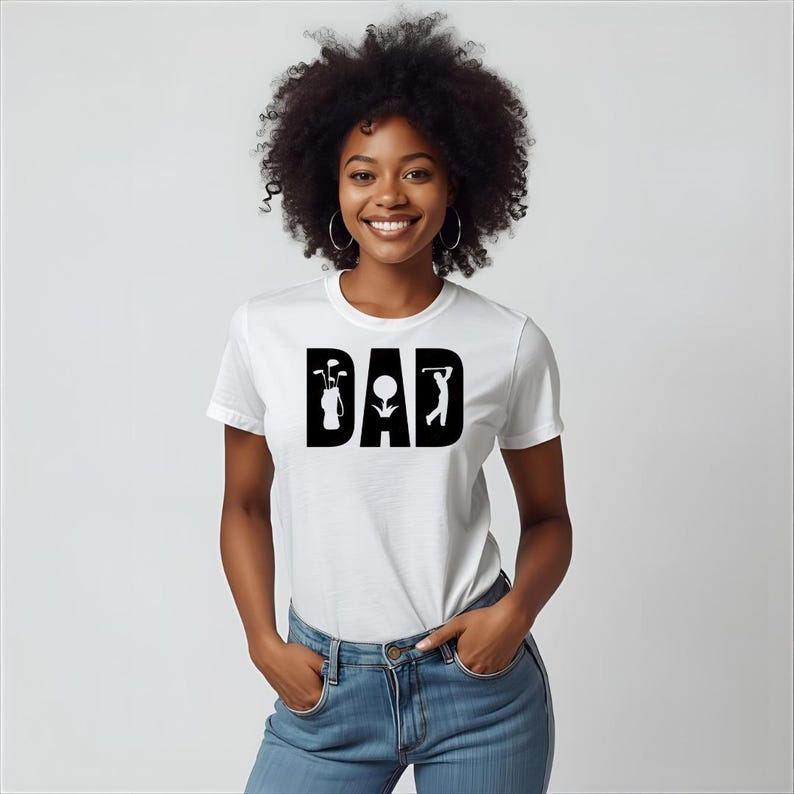 May include: White t-shirt with the word "DAD" in bold black letters. The letter "D" features a golf bag with clubs, the "A" has a golf ball, and the final "D" shows a golfer swinging.