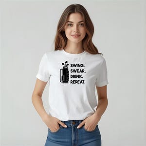 May include: White t-shirt with a black graphic of a golf bag and clubs, and the text "SWING. SWEAR. DRINK. REPEAT." The shirt has short sleeves and a crew neck.