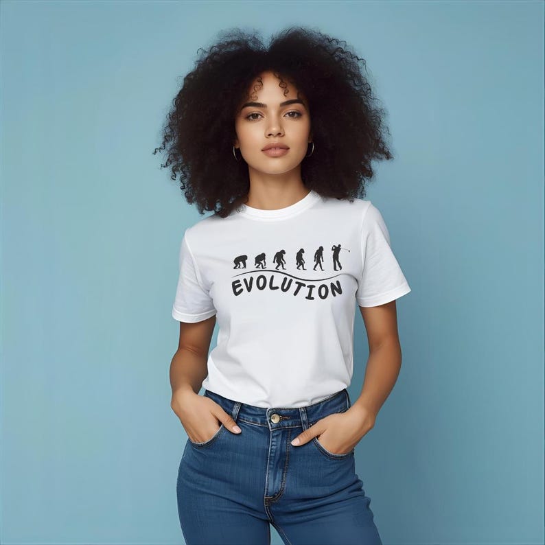 May include: White t-shirt with a black graphic depicting the evolution of a golfer. The word "EVOLUTION" is printed below the graphic in a curved font. The model is wearing blue jeans.