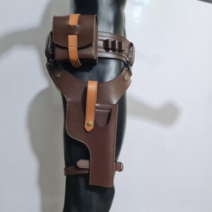 Puede incluir: Una funda de muslo de cuero marr&oacute;n con cintur&oacute;n y bolsa a juego. La funda presenta un bolsillo para pistola, una trabilla para el cintur&oacute;n y una correa que se asegura alrededor del muslo. La bolsa y la funda tienen detalles en color beige.