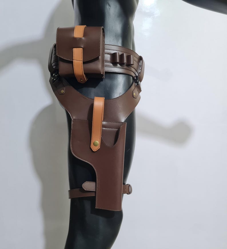 Puede incluir: Una funda de muslo de cuero marr&oacute;n con cintur&oacute;n y bolsa a juego. La funda presenta un bolsillo para pistola, una trabilla para el cintur&oacute;n y una correa que se asegura alrededor del muslo. La bolsa y la funda tienen detalles en color beige.