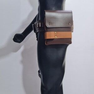 Puede incluir: Un cintur&oacute;n de cuero marr&oacute;n con una bolsa a juego. La bolsa es rectangular con una solapa y una correa marr&oacute;n claro. El cintur&oacute;n tiene m&uacute;ltiples trabillas y una hebilla. El dise&ntilde;o es robusto y funcional. La bolsa est&aacute; sujeta al cintur&oacute;n.