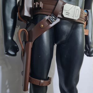 Puede incluir: Cintur&oacute;n utilitario de cuero marr&oacute;n con una funda y una correa para la pierna. El cintur&oacute;n presenta una hebilla plateada y m&uacute;ltiples bolsas. La funda est&aacute; dise&ntilde;ada para guardar un arma. El cintur&oacute;n se usa en un maniqu&iacute; negro.