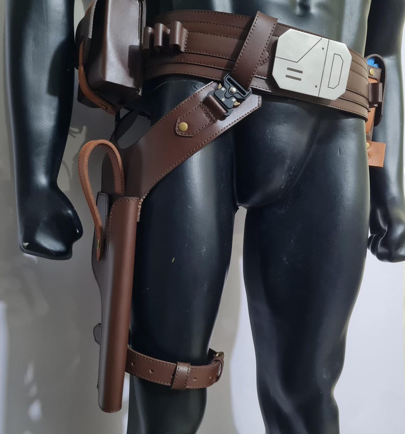 Puede incluir: Cintur&oacute;n utilitario de cuero marr&oacute;n con una funda y una correa para la pierna. El cintur&oacute;n presenta una hebilla plateada y m&uacute;ltiples bolsas. La funda est&aacute; dise&ntilde;ada para guardar un arma. El cintur&oacute;n se usa en un maniqu&iacute; negro.