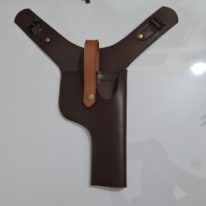 Puede incluir: Una funda de hombro de cuero marr&oacute;n con una funda vertical para una pistola. La funda tiene una correa de cuero marr&oacute;n claro y herrajes de color lat&oacute;n. Las correas de los hombros son ajustables y tienen hebillas.