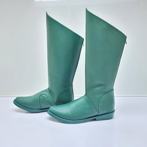 Puede incluir: Un par de botas altas de color verde azulado. Las botas tienen un diseño único con una parte superior inclinada y una cremallera en la parte trasera. Están hechas de un material liso y tienen una suela plana.