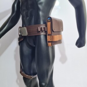 Puede incluir: Cintur&oacute;n utilitario de cuero marr&oacute;n con una bolsa rectangular y una hebilla plateada. El cintur&oacute;n presenta una serie de peque&ntilde;os lazos y una correa para la pierna. La bolsa tiene una correa marr&oacute;n claro y est&aacute; asegurada con dos remaches color lat&oacute;n.