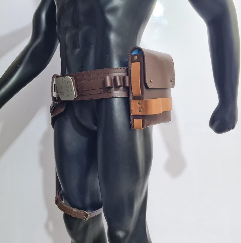 Puede incluir: Cintur&oacute;n utilitario de cuero marr&oacute;n con una bolsa rectangular y una hebilla plateada. El cintur&oacute;n presenta una serie de peque&ntilde;os lazos y una correa para la pierna. La bolsa tiene una correa marr&oacute;n claro y est&aacute; asegurada con dos remaches color lat&oacute;n.