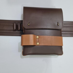 Puede incluir: Un cintur&oacute;n de cuero marr&oacute;n con una bolsa a juego y una correa marr&oacute;n m&aacute;s clara. La bolsa tiene un cierre de solapa con remaches de lat&oacute;n. El cintur&oacute;n tambi&eacute;n presenta una hebilla plateada y peque&ntilde;os bucles.