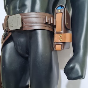 Puede incluir: Un cintur&oacute;n utilitario de cuero marr&oacute;n con una hebilla plateada y una funda a juego. La funda es de dos tonos, con un acento marr&oacute;n m&aacute;s claro y remaches de lat&oacute;n. El cintur&oacute;n lo lleva un maniqu&iacute;.