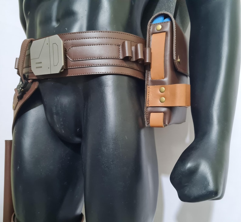 Puede incluir: Un cintur&oacute;n utilitario de cuero marr&oacute;n con una hebilla plateada y una funda a juego. La funda es de dos tonos, con un acento marr&oacute;n m&aacute;s claro y remaches de lat&oacute;n. El cintur&oacute;n lo lleva un maniqu&iacute;.