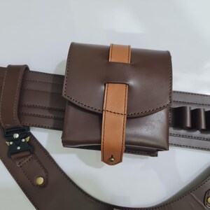 Puede incluir: Un cintur&oacute;n utilitario de cuero marr&oacute;n con una bolsa y soportes adicionales. La bolsa tiene un cierre de solapa con un acento de cuero marr&oacute;n claro. El cintur&oacute;n presenta una hebilla y correas ajustables. El dise&ntilde;o general es funcional y resistente.
