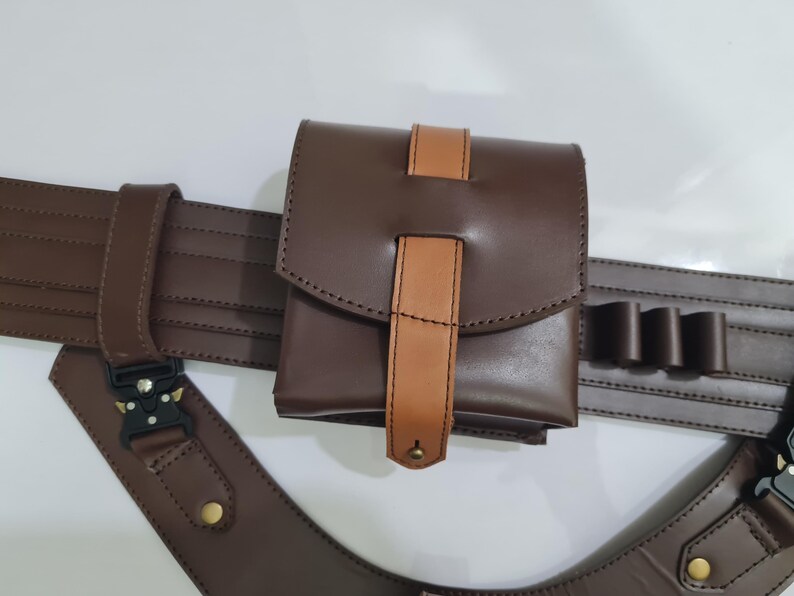 Puede incluir: Un cintur&oacute;n utilitario de cuero marr&oacute;n con una bolsa y soportes adicionales. La bolsa tiene un cierre de solapa con un acento de cuero marr&oacute;n claro. El cintur&oacute;n presenta una hebilla y correas ajustables. El dise&ntilde;o general es funcional y resistente.