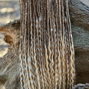 May include: A set of long, wavy synthetic dreadlocks in shades of brown and blonde. The dreadlocks are decorated with small silver beads.