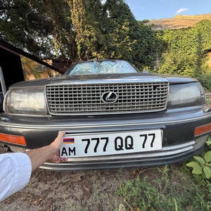 May include: A dark gray Lexus sedan with a chrome grille and headlights. The front license plate reads "777 QQ 77" with the letters "AM" and the Armenian flag. The car is parked outdoors.