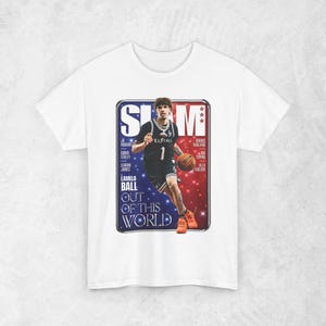 以下が含まれることがあります： バスケットボール選手が描かれた白いTシャツ。「SLAM」と「LAMELO BALL OUT OF THIS WORLD」の文字が入っています。バスケットボールのユニフォームを着た選手の写真がデザインされています。