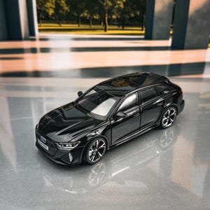 May include: A black Audi RS6 model car with a glossy finish. The miniature car has detailed features, including a sunroof, alloy wheels, and a front license plate. The car is displayed on a reflective surface.