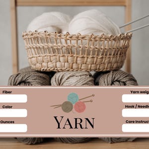 May include: A wicker basket holds two large white yarn balls, placed above several grey yarn skeins. Knitting needles are in the basket. A label at the bottom reads "YARN" with spaces for fiber, colour, ounces, yarn weight, hook/needle size, and care instructions.