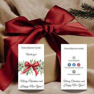 Puede incluir: Un regalo envuelto con un gran lazo de sat&eacute;n burdeos. Se ven dos tarjetas blancas, una con un lazo y vegetaci&oacute;n de acuarela, la otra con iconos de redes sociales. El texto de las tarjetas dice "&iexcl;Feliz Navidad y Pr&oacute;spero A&ntilde;o Nuevo!"