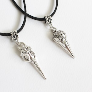 May include: Two black cord necklaces with silver bird skull pendants. The pendants have intricate details and a pointed beak.