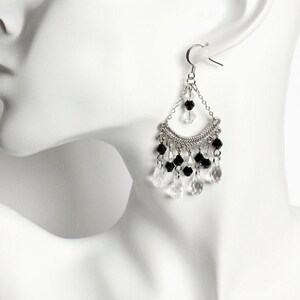 May include: Silver dangle earrings with black and clear crystal beads. The earrings have a teardrop shape and are accented with a silver chain.