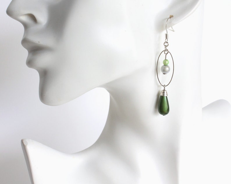 Puede incluir: Pendientes de plata con una cuenta verde en forma de l&aacute;grima y un aro de plata con una cuenta verde y blanca.
