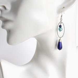 Puede incluir: Pendientes de plata con una perla azul en forma de l&aacute;grima y una perla azul m&aacute;s peque&ntilde;a en un aro ovalado de plata.