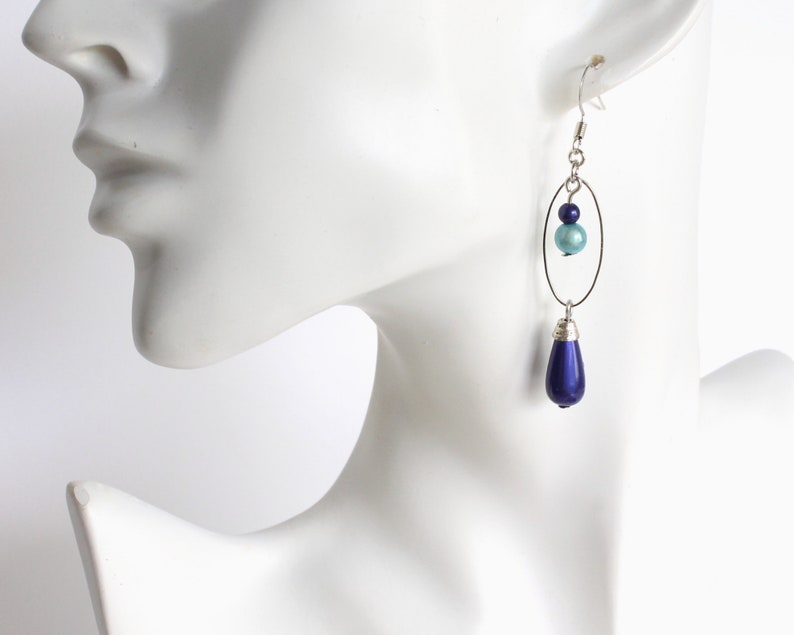Puede incluir: Pendientes de plata con una perla azul en forma de l&aacute;grima y una perla azul m&aacute;s peque&ntilde;a en un aro ovalado de plata.