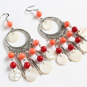 Könnte beinhalten: Ein Paar silberne Creolen mit einem hängenden Design. Die Ohrringe haben rote und orange Perlen, weiße Muschelaccente und silberne Federn.
