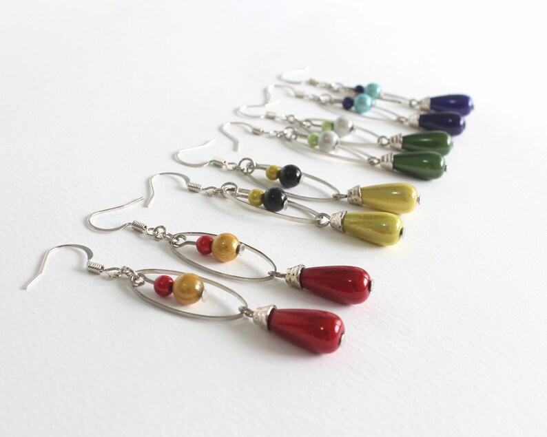 Puede incluir: Un conjunto de pendientes colgantes con aros plateados y cuentas de vidrio de colores. Los pendientes presentan una variedad de colores, incluyendo rojo, amarillo, verde, azul y negro.