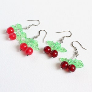 May include: A pair of silver dangle earrings with red cherry charms and green leaf accents.